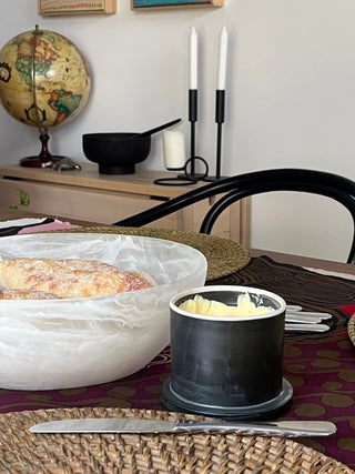 black butter bell on rustic dining table beside a white bowl of bread