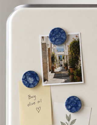 Two side-by-side views of a white refrigerator door showing round blue marbled magnetic notes and clips holding sticky notes, a photo, and a card.